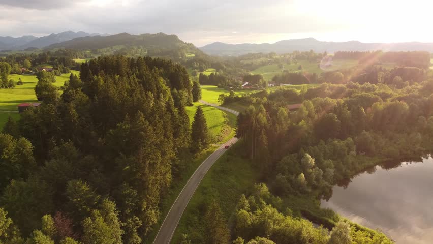 4k drone shot of a red car driving in the golden hour through a beautiful green landscape.
