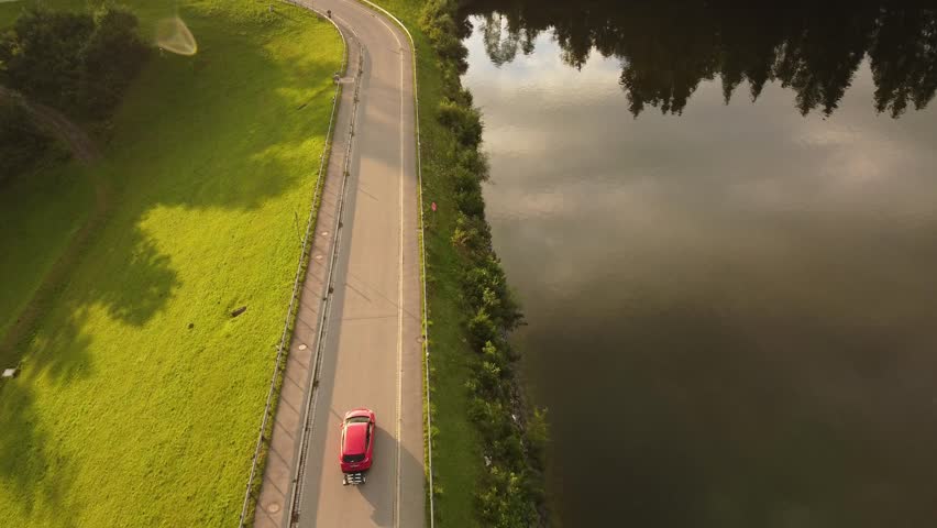 4k drone shot of a red car driving in a hilly Landscape.