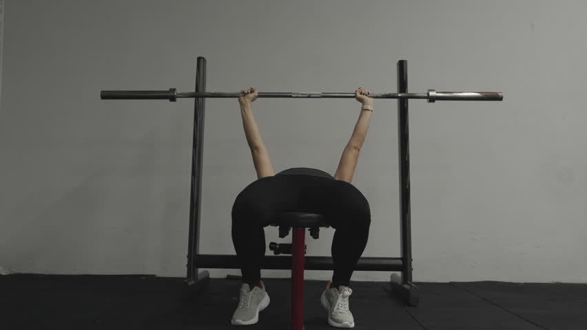 Woman presses an empty barbell with her hands while lying on the bench in the gym. Royalty-Free Stock Footage #1111099551