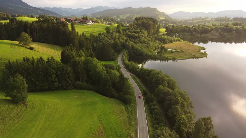 4k drone shot of a red car driving in the golden hour through a beautiful green landscape.