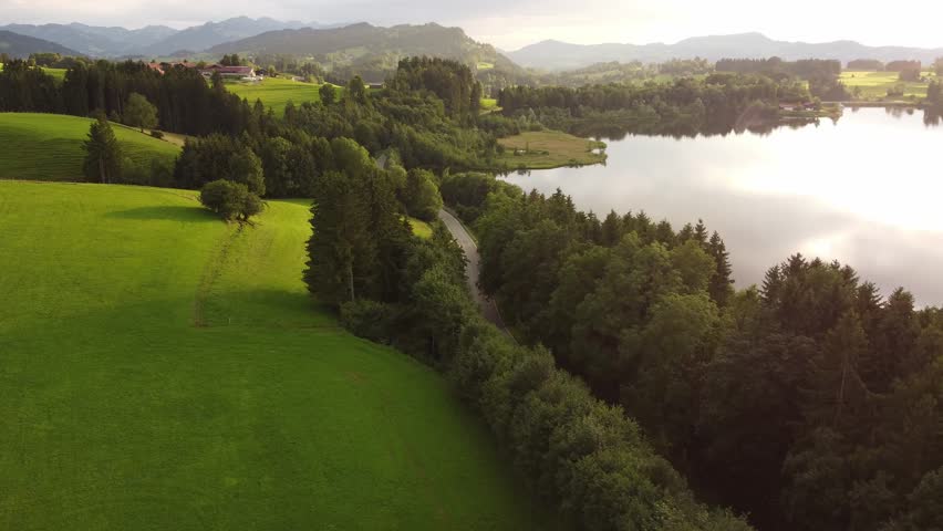 4k drone shot of a red car driving in the golden hour through a beautiful green landscape.