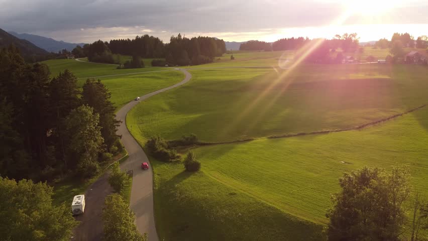 4k drone shot of a red car driving in the golden hour through a beautiful green landscape.