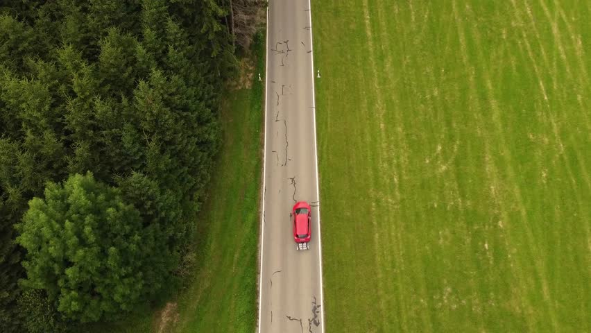 4k drone shot of a red car driving in a hilly Landscape.