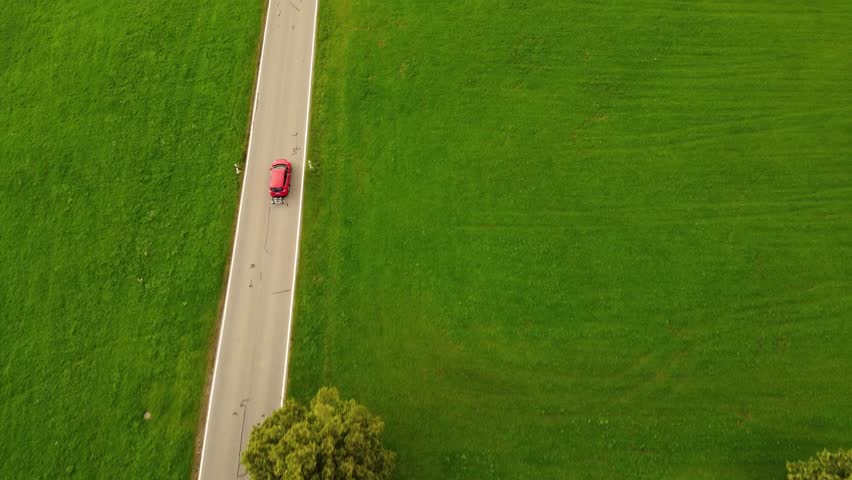 4k drone shot of a red car driving in a hilly Landscape.