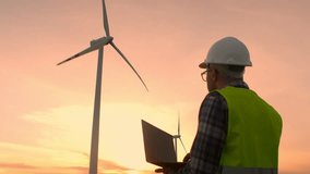 Man maintenance engineer works at a wind farm at sunset with a laptop in his hands. Green ecological power energy generation wind sustainable energy concept. - Powered by Shutterstock - Get 15% off with code: PIKWIZARD15