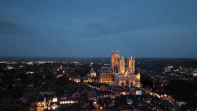 Aerial drone video captures the renowned Lincoln Cathedral in Lincolnshire, UK, at dusk, showcasing its majestic Gothic architecture with illumination.