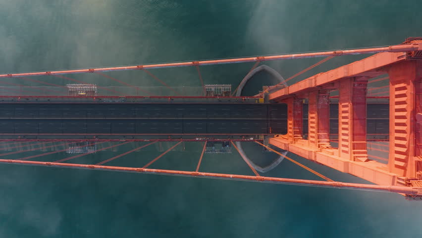 Overhead view of Golden Gate Bridge, San Francisco in misty golden sunset light. View from top to bottom deep blue ocean and tall red construction of California landmark USA Golden Gate Bridge aerial Royalty-Free Stock Footage #1111108359