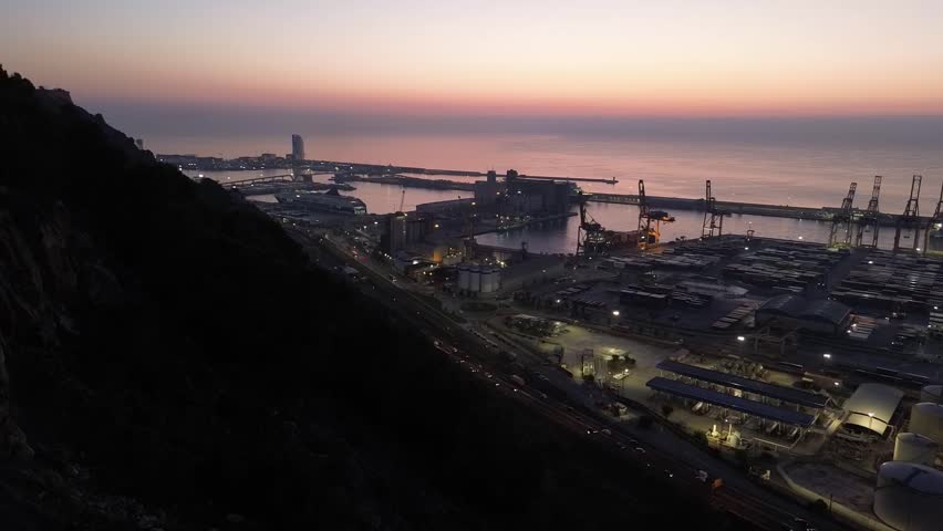 Nighttime drone hyperlapse of a city port with streaming car lights on the road, epitomizing a frenetic urban port life. Copyspace included.