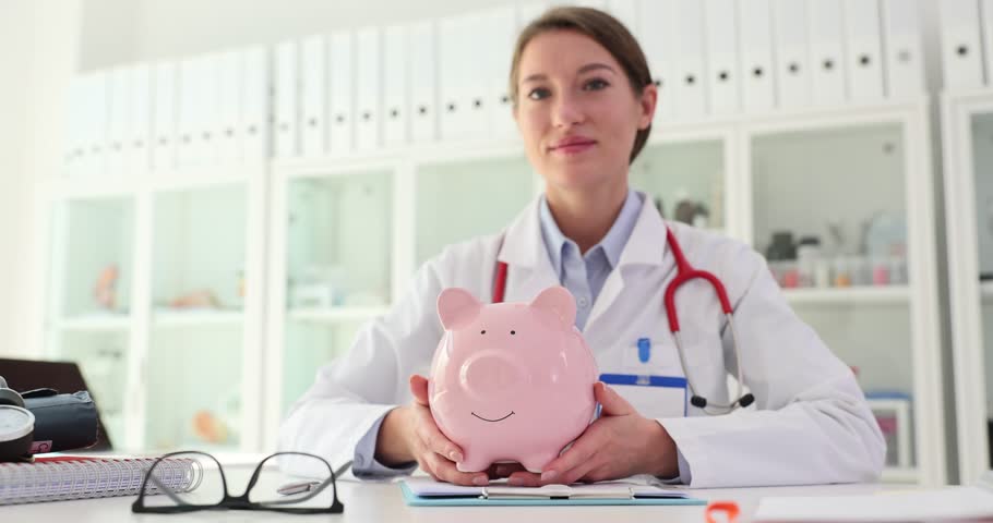 Doctor therapist with pink piggy bank in hands in clinic. Expensive medical procedures and investments in health and health insurance costs Royalty-Free Stock Footage #1111113495
