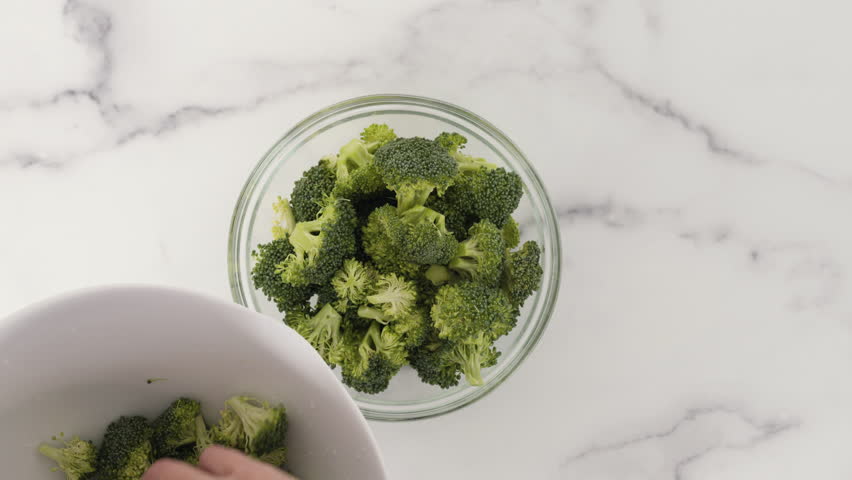 Raw organic broccoli florets in a glass bowl close-up on a marble background