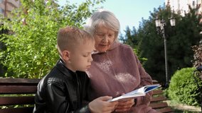 A loving great-grandmother reads a book with her grandson sitting on a bench in the yard in autumn. The grandson spends time with an elderly grandmother. - Powered by Shutterstock - Get 15% off with code: PIKWIZARD15