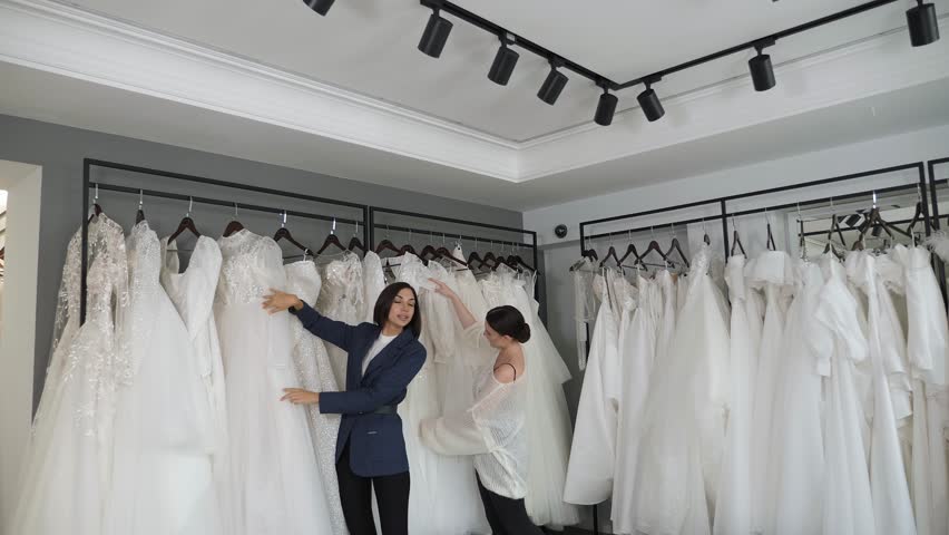 Two happy young women choose a wedding dress in a modern wedding showroom. Two brides are buying a dress at a wedding salon. Preparation for the wedding. Royalty-Free Stock Footage #1111119567