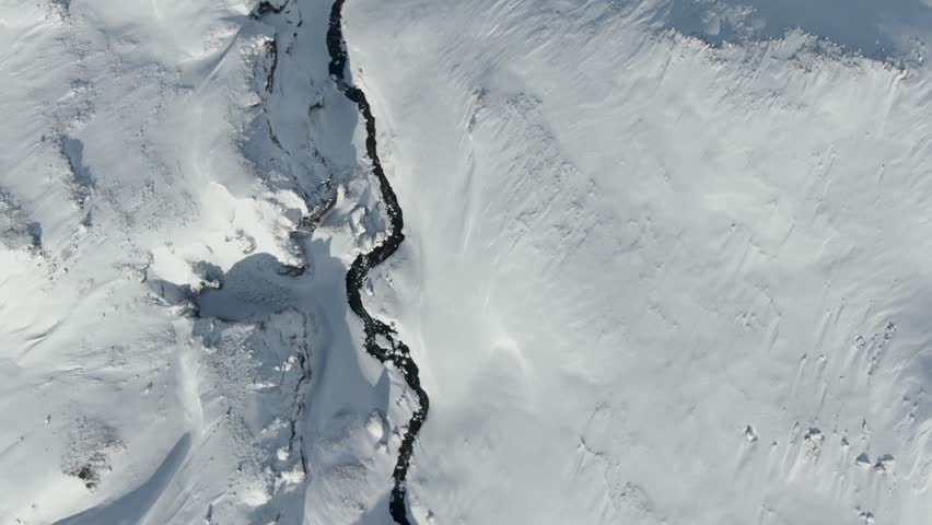 Nature of the North. Mountain river . Top-down aerial view of a winding river cutting through a snow-covered landscape. Minimal winter scene with dark water contrasting against white snow, creating natural abstract pattern.