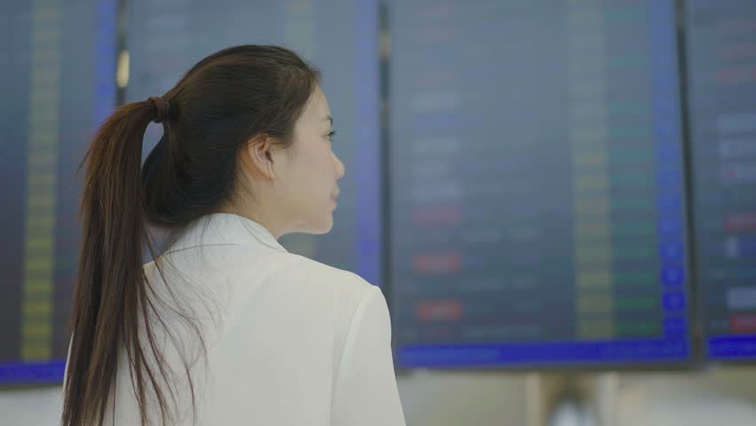 Young asian woman with passport and boarding pass as a hand stand in front of the airline time schedule board looking at the flight information board at the airport terminal, checking her flight Royalty-Free Stock Footage #1111125005