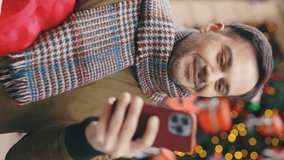 Vertical video. Handsome man walking in the street holding the valentino heart shape gift using smartphone. Smiled man outside with the red christmas present texting, scrolling