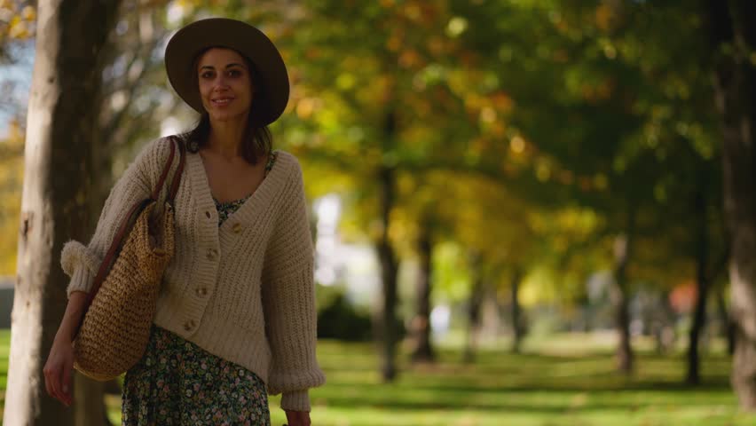 woman wearing hat and long sweater or cardigan walks through natural maple park with golden foliage. Woman in nature at warm day. Active lifestyle. People in forest. Tourist walk in autumn park Royalty-Free Stock Footage #1111128031