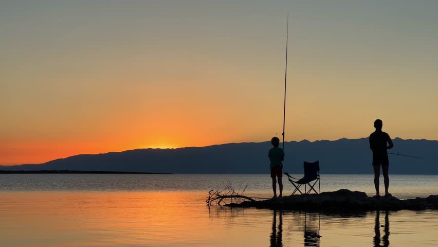 Fishermen at sunset of Issyk-Kul mountain lake, Kyrgyzstan. The sun goes behind the mountains at sunset. Calm, peaceful natural background. Lake with a view of the Tien Shan Mountains. Kyrgyzstan 4K