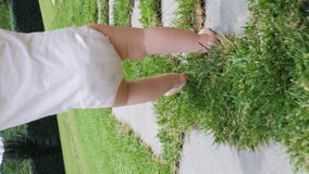 Vertical video. Young mother guiding her baby to walk in summer park, barefoot on the grass, slow motion