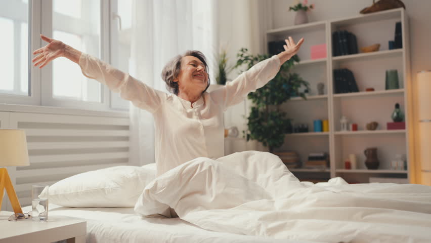 Smiling senior woman waking up in bed and stretching, morning rituals , health