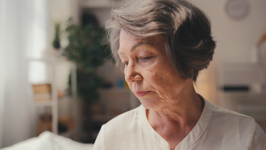 Sad senior woman taking pills with water, feeling tired of everyday medication