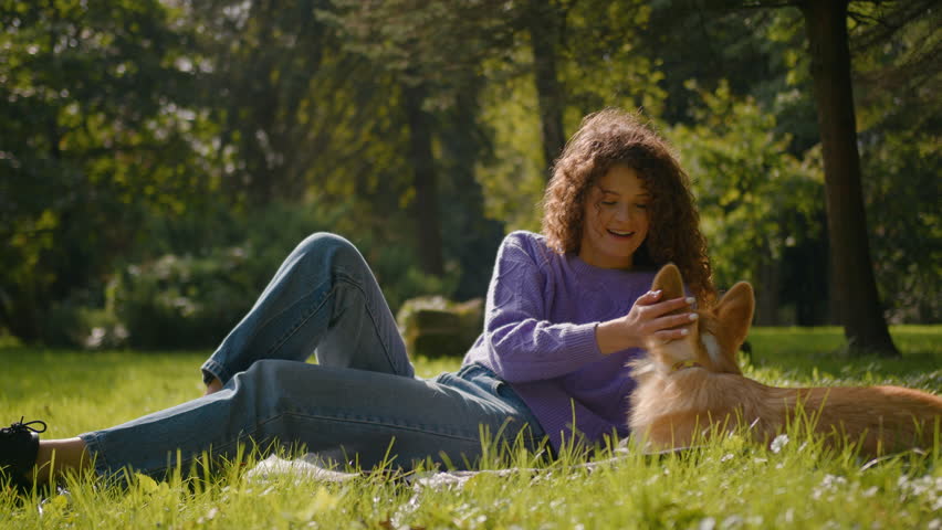 Outdoors rest young woman pets friendly owner caress lovely puppy happy gen z girl playing with welsh corgi dog loyal domestic pet scratching doggy love animal having fun together in city park lawn Royalty-Free Stock Footage #1111135975