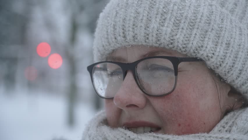 Portrait of woman in warm clothes wearing glasses with snow drops on lenses during winter snowstorm. Discomfort and dissatisfied facial expression with negative emotions in bad weather, closeup. Royalty-Free Stock Footage #1111136659