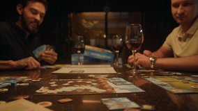At the table some people are playing a board game. One of the men throws the dice twice. Another man watches it attentively. A woman takes a glass of wine from the table, drinks it, and puts it back. - Powered by Shutterstock - Get 15% off with code: PIKWIZARD15