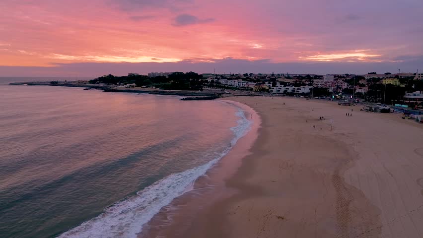 Aerial drone a view of the oceanfront city beach during a colorful romantic pink sunset, Lisbon, Portugal. High quality FullHD footage