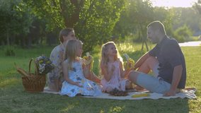 Caucasian family with cute blonde little girls in park in summer. Happy childhood. Happy children are eating fruits sitting on blanket outside. Real time. Family weekend. Kids eat bananas on nature - Powered by Shutterstock - Get 15% off with code: PIKWIZARD15