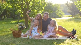 Happy family having picnic sitting on blanket in park on sunny day and taking selfie photos on smartphone. Young cheerful parents taking pictures with kids on mobile phone outdoor. Real time. - Powered by Shutterstock - Get 15% off with code: PIKWIZARD15