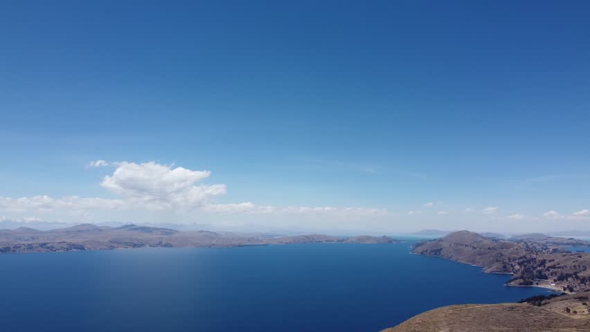 Camera panning from one shoreline to another across the deep blue waters of Lake Titicaca Bolivia with snow capped cone shaped mountain in the background