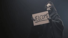 Grim reaper holding a Welcome sign and luring people to him, dancing, on the black background. Mysticism and the afterlife. - Powered by Shutterstock - Get 15% off with code: PIKWIZARD15
