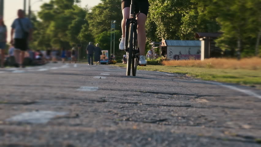 Woman on a bicycle rides along the bike path in the park during sunset in slow motion. Girl cycling on city embankment. Concept of enjoying life, cheerfulness, healthy lifestyle