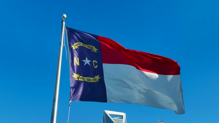 North Carolina flag waving against bright blue sky. Static aerial shot in downtown city in NC.