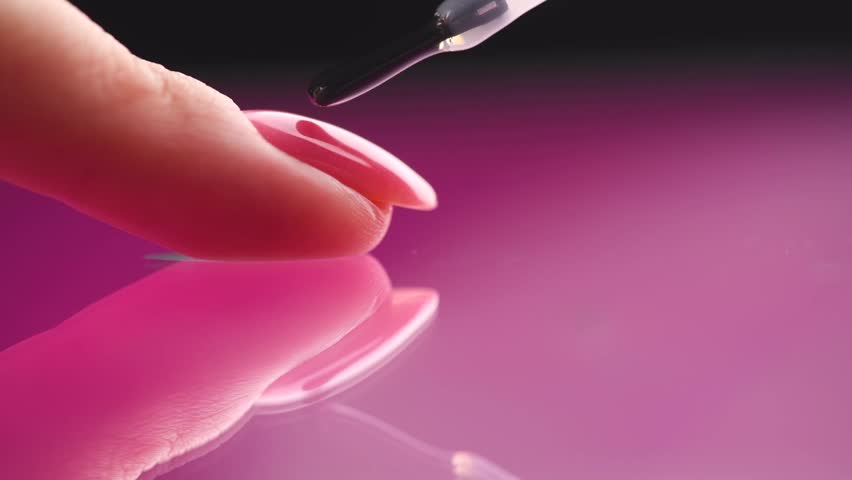 Applying Nail polish, pink shellac UV gel, varnish, manicure process concept in beauty salon. Transparent top coat drop on brush. Over pink background. Application of nail polish Royalty-Free Stock Footage #1111172517