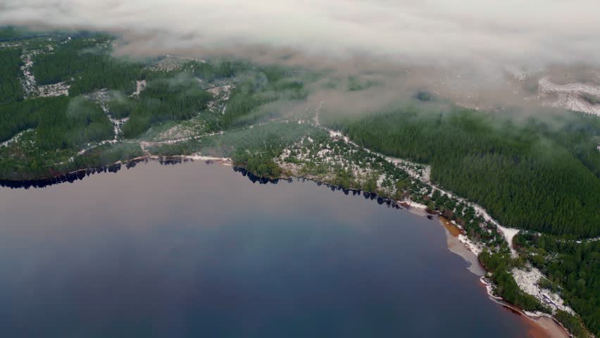Above verdant forest around lake shrouded in cloud surrounded by snowy mountains 