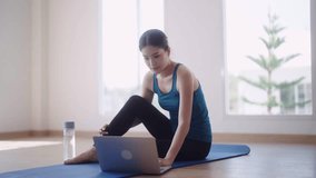 Asian female fitness trainer in workout is conducting online fitness classes through video call on her laptop to help students maintain their strength and good health while exercising at home