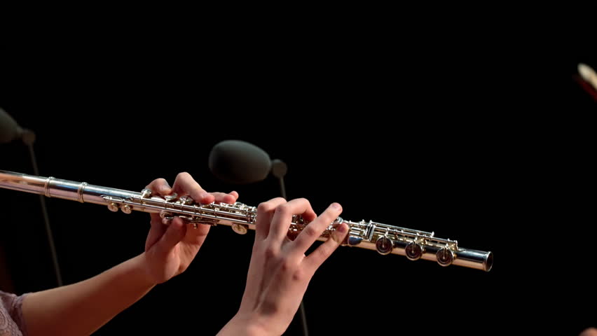 Flute in female hands against microphone background and dark background. A female soloist plays the flute