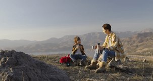 Mother and kid conquer mountain, trekking poles backpacks. Healthy lifestyle mother and child hiking. Mother and son conversations. Joyful faces while relaxing on rocks. Relaxing in nature, mountains