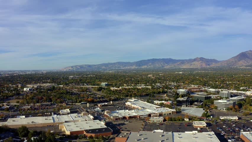 Left trucking aerial drone extreme wide landscape shot of the Salt Lake county valley covered in buildings, busy roads, and colorful autumn trees on a warm sunny fall evening in Utah