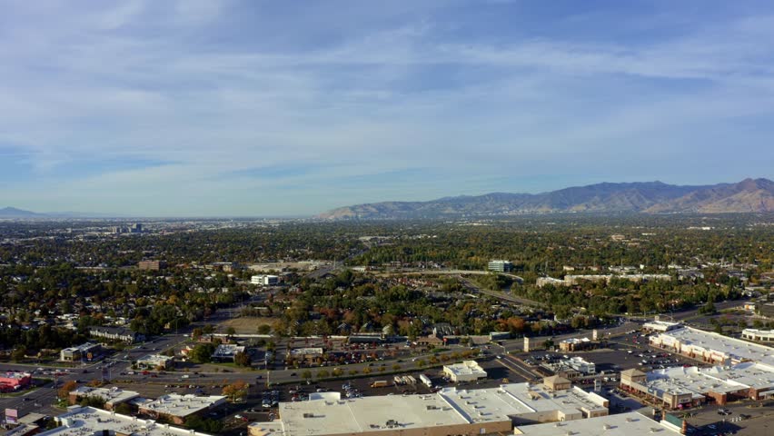 Left trucking aerial drone extreme wide landscape shot of the Salt Lake county valley covered in buildings, busy roads, and colorful autumn trees on a warm sunny fall evening in Utah