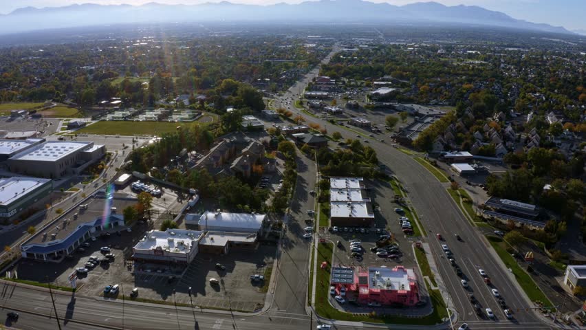 Dolly in tilt up aerial drone extreme wide landscape shot of the Salt Lake county valley covered in buildings, busy roads, and colorful autumn trees surrounded by mountains on a fall evening in Utah