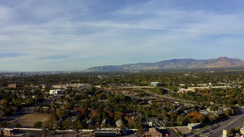 Right trucking rising aerial drone extreme wide landscape shot of the Salt Lake county valley covered in buildings, busy roads, and colorful autumn trees on a warm sunny fall evening in Utah