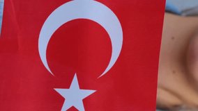 Caucasian teenage girl in red t-shirt and denim jacket keeping small flag of Turkey in her hands. Young female is standing outdoors, smiling and waving small Turkish flag. Real time. Vertical video.