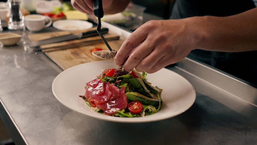 The chef of the Italian restaurant decorates the dish, lays out the ingredients with tongs which he prepared in professional kitchen