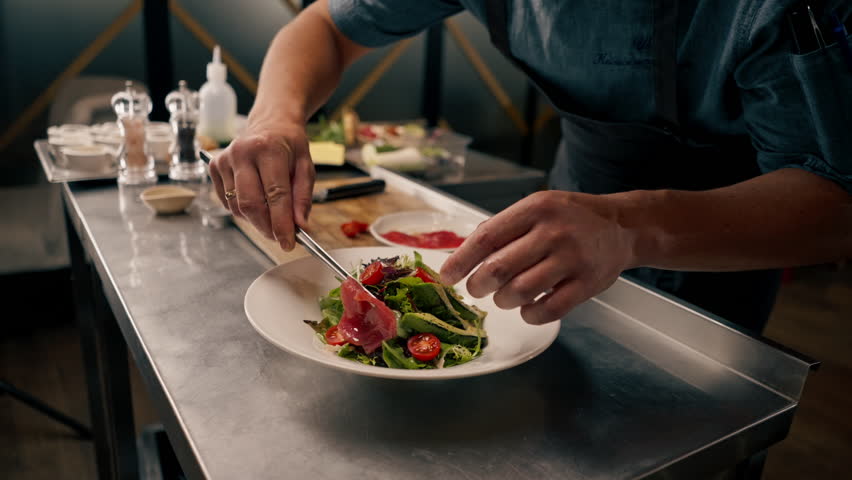 The chef of the Italian restaurant decorates the dish, lays out the ingredients with tongs which he prepared in professional kitchen