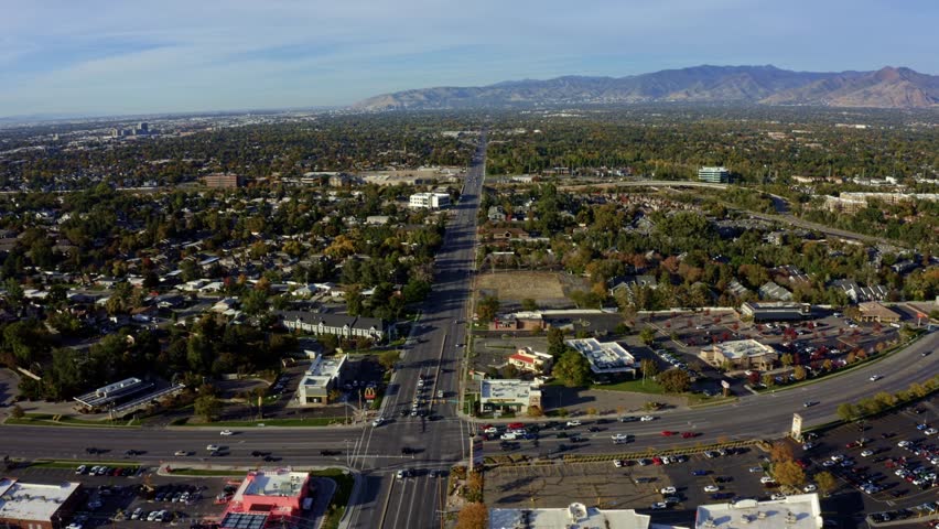 Dolly in tilt up aerial drone extreme wide landscape shot of the Salt Lake county valley covered in buildings, busy roads, and colorful autumn trees on a warm sunny fall evening in Utah