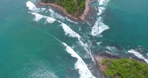 Drone video tilting down over Playa Herradura where two islands nearly touch leaving a gap for the Pacific Ocean water to flow