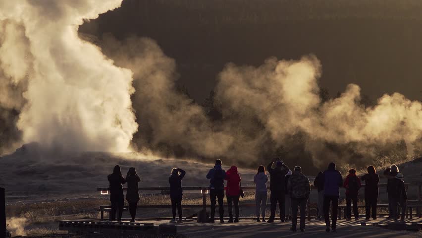 Close up of tourists, the eruption of Old Faithful Geyser at sunrise, Yellowstone National Park, Wyoming, USA