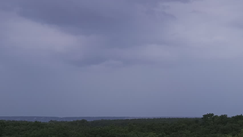 Lightning flash in storm clouds. Heavy clouds bring multiple flashes of lightning and thunderstorm. Big bolts of lightning strike at evening sky above the forest horizon. Slow Motion. 4K